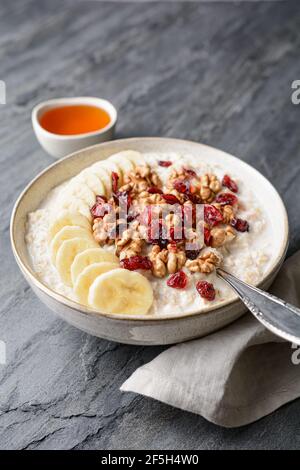 Healthy cereal breakfast, oatmeal topped with banana slices, dried cranberries, walnut, served with honey in a bowl Stock Photo