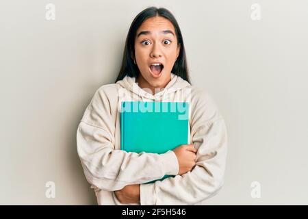 Young asian woman holding book afraid and shocked with surprise and amazed expression, fear and excited face. Stock Photo