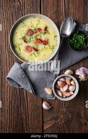 Caldo Verde soup made of savoy cabbage, pureed potatoes, onion, garlic and fried sausage slices in a ceramic bowl  on rustic wooden background Stock Photo