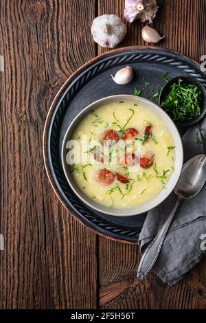 Caldo Verde soup made of savoy cabbage, pureed potatoes, onion, garlic and fried sausage slices in a ceramic bowl  on rustic wooden background Stock Photo
