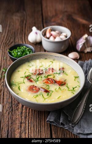 Caldo Verde soup made of savoy cabbage, pureed potatoes, onion, garlic and fried sausage slices in a ceramic bowl  on rustic wooden background Stock Photo