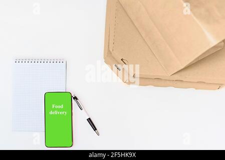 Paper bag and pizza delivery boxes on white table background, phone green screen, note. Mockup for design, copy spase. Stock Photo