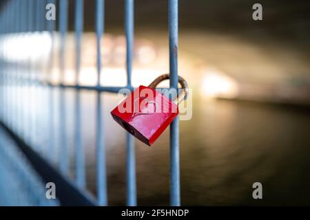 a red padlock on which is engraved a heart hangs on a fence Stock Photo