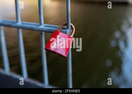 a red padlock on which is engraved a heart hangs on a fence Stock Photo