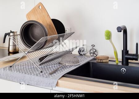 Modern kitchen sink with drying rack holding cookware, chopping board and utensils after washing, clean domestic interior. Stock Photo