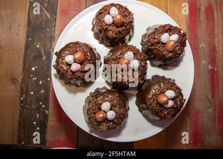 A selection of Easter Chocolate nest Cakes topped with three little chocolate mini eggs on a white plate Stock Photo