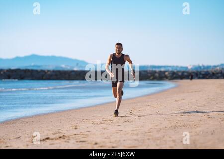 Runner in motion. Young sporty athletic man running along the beach Stock Photo