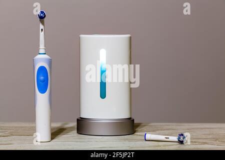 Close up isolated image of an ultraviolet toothbrush head sterilizer device that is working in the middle with electric toothbrush on the left an a sp Stock Photo