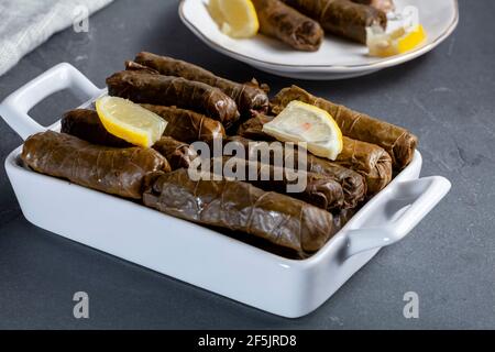 Yaprak sarmasi is a traditional Turkish dish made by wrapping rice stuffing with grape leaves.  A tray of hand rolled sarmas are served on stone backg Stock Photo