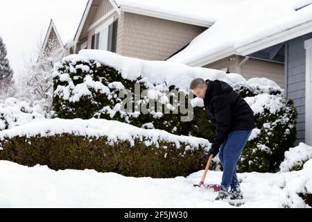 Mature man shoveling snow off sidewalk in front of home Stock Photo