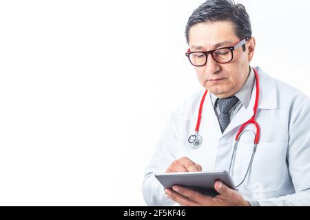 Latino doctor in white coat, glasses, stethoscope and tie checking his tablet on white background. Medical technology concept Stock Photo