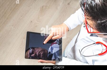 Top view of a doctor in a white coat, tie and stethoscope working on his tablet. Technology and medicine concept Stock Photo