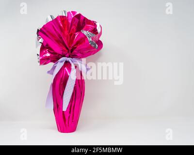 Giant chocolate Easter egg wrapped in pink silver foil with a pretty purple polka dot bow. Horizontal, white background Stock Photo