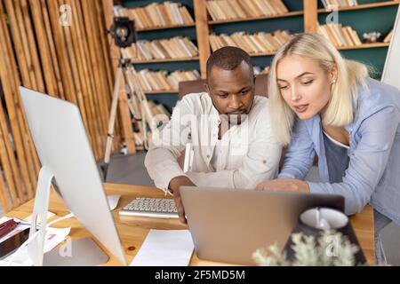 Concentrated business partners using laptop, working on new strategy for company. Serious multiracial coworkers searching and discussing ideas for Stock Photo