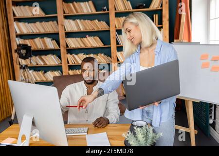 Multiethnic stylish employees using computer, discussing ideas for project. Friendly successful colleagues working on new business strategy together Stock Photo