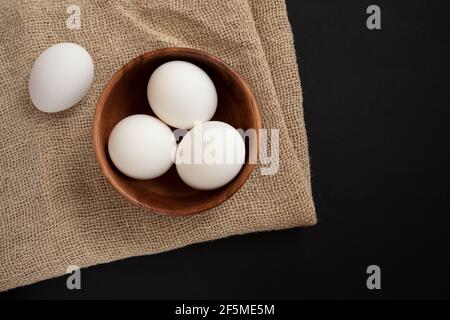 Fresh chicken eggs in a wooden plate on a wooden table background.
