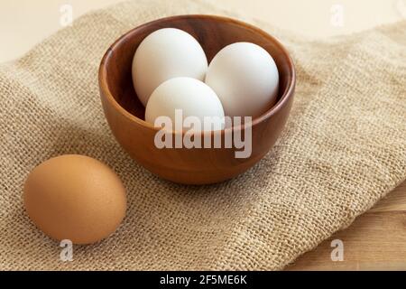Fresh chicken eggs in a wooden plate on a wooden table background. Stock Photo