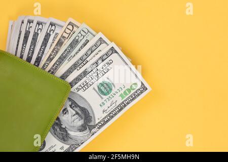Green leather wallet with hundred-dollar bills on a yellow background. Stock Photo