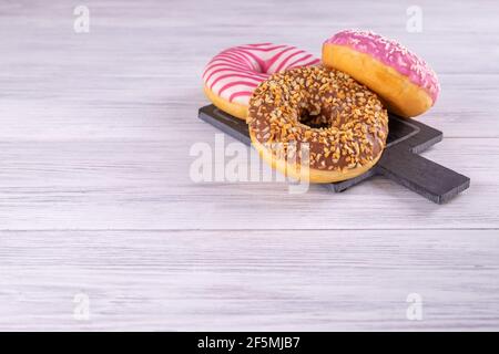 Three iced donuts are stacked on a pink black slate serving board Stock Photo
