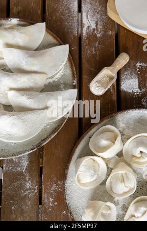 Raw homemade dumplings on two plates on a dark wooden table. Stock Photo
