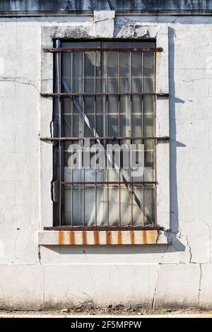 An old window with rusty bars set in a rough wall Stock Photo