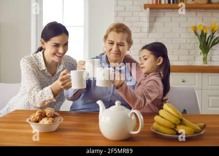 Three generations of women of one family drinking tea together sitting at home in the kitchen.