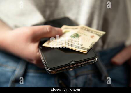 The girl is holding money and a phone in her hand. The woman has cash and a mobile phone in her hand. At close range. Modern technologies. Stock Photo