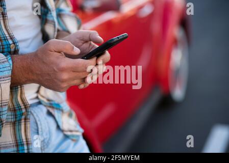 Close up of man using phone outdoor - unrecognizable people with cellular smartphone chatting or texting with car in background - modern lifestyle wit Stock Photo