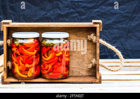 Closeup shot of glass jars with pickled red peppers in a wooden crate Stock Photo