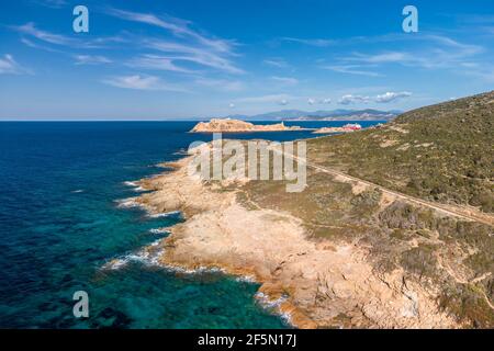 Ile Rousse, Corsica, France - 23rd March 2021. A Corsica Linea ferry waits in the harbour at Ile Rousse with the railway track winding along the rugge Stock Photo