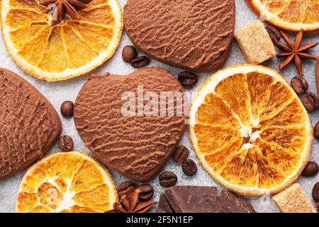 Chocolate heart cookies, oranges cinnamon and spicy spices on a gray table, top view, close up Stock Photo