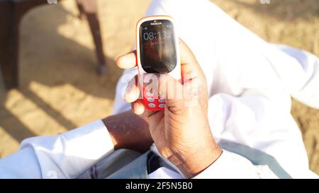Rajasthan, India - March 20, 2021; A man holding Nokia keypad mobile model 3310 with black screen isolated on white background. Smartphone key press i Stock Photo