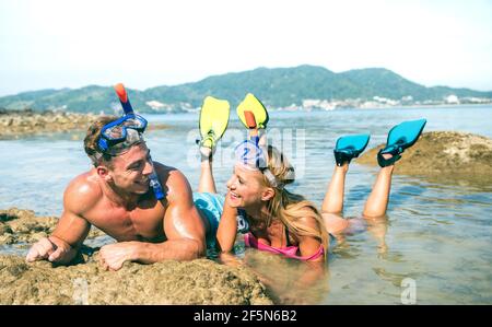 Happy couple of vacationer in love having fun at water on tropical beach in Thailand with snorkel mask and fins - Active youth travel concept Stock Photo