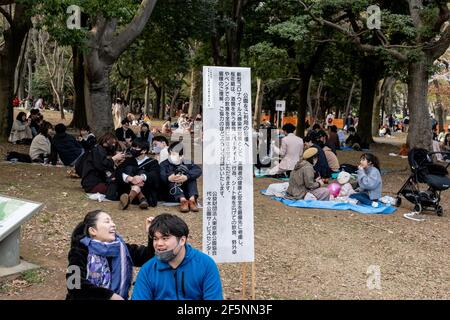 Tokyo, Japan. 27th Mar, 2021. People enjoying a picnic under cherry blossom trees (sakura) at the Yoyogi Park in Tokyo.Sakura area is blocked by the orange lines to avoid crowds gathering nearby. People enjoy the cherry blossom from a distance. Japanese government ended the state of emergency on 21st March, but urged people not to gather to prevent a resurgence of COVID-19 infections. (Photo by Viola Kam/SOPA Images/Sipa USA) Credit: Sipa USA/Alamy Live News Stock Photo