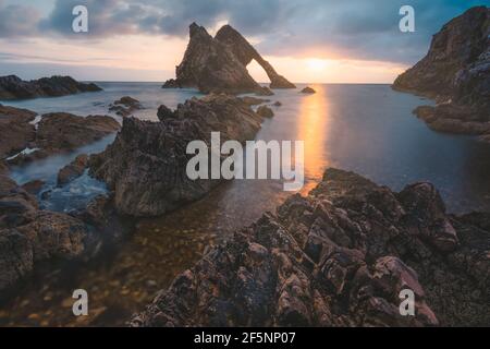 Beautiful dramatic sescape scenery at sunrise or sunset of Bow Fiddle Rock sea arch on the rocky shore of Portknockie on the Moray Firth in Scotland. Stock Photo