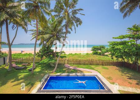 A young female tourist floats in a relaxing pool while on a tropical beach vacation in Weligama, Sri Lanka. Stock Photo