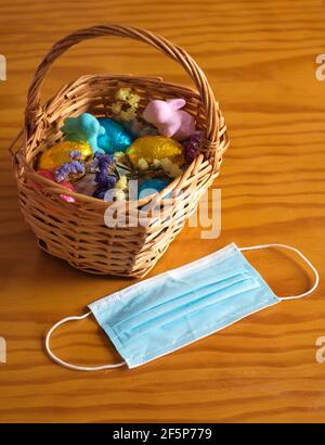 Basket with easter eggs, bunnies and flowers on a wooden table. Facial mask outside the basket Stock Photo