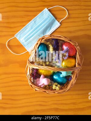 Basket with easter eggs, bunnies and flowers on a wooden table. Facial mask outside the basket Stock Photo