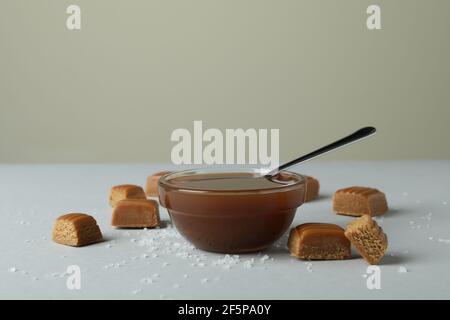 Salted caramel pieces and bowl of sauce on light gray table Stock Photo