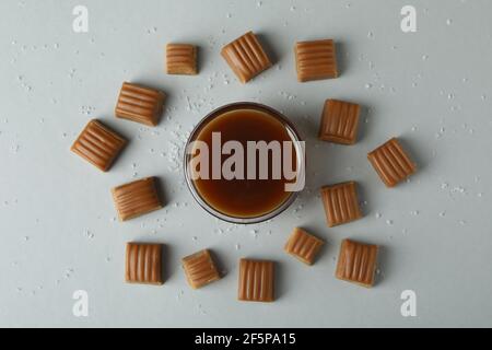 Salted caramel pieces and bowl of sauce on light gray background Stock Photo