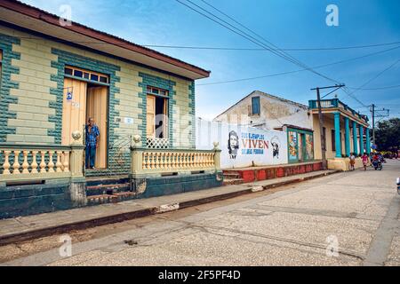 Baracoa, Cuba - October 25, 2019:  Old cuban man in front of his accommodation (casa particular) in Baracoa with painted communist propaganda and Che Stock Photo