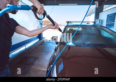 Man washing car in self serve car wash. Cleaning car using high pressure water. Car smart wash Stock Photo