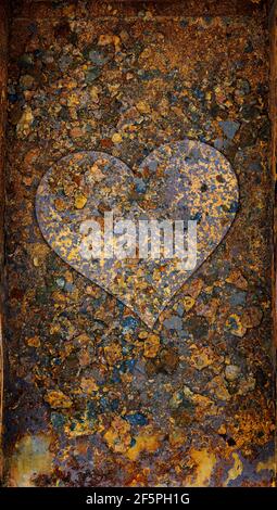 Rusty metal heart on corroded and rusting steel ash pan. After years of use and exposure to heat and solid fuel ash the pan was left out in th erain f Stock Photo