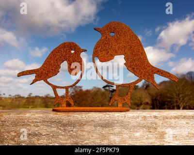 A decorative pair of robins laser cut in rusting steel mounted on a wooden base with light cloud and blue sky behind Stock Photo