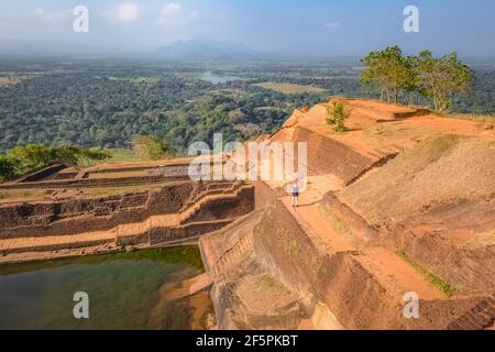 A lone blonde caucasian female backpacker tourist visits the terraced gardens  atop the ancient historic Sigiriya Rock Fortress or Lion Rock in Sri La Stock Photo