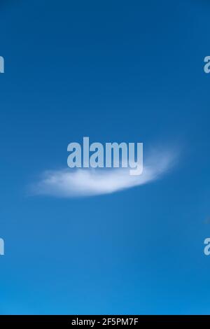 A single white cloud set against a bright blue sunny sky in a vertical image Stock Photo