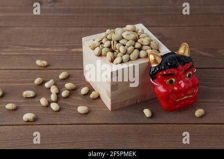 parched soy beans in measuring box with demon mask isolated on wooden table Stock Photo