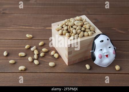 parched soy beans in measuring box with demon mask isolated on wooden table Stock Photo