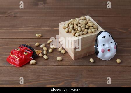parched soy beans in measuring box with demon mask isolated on wooden table Stock Photo