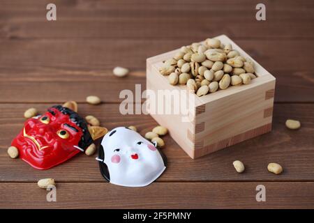 parched soy beans in measuring box with demon mask isolated on wooden table Stock Photo